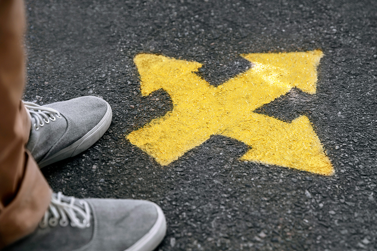 Sneakered feet standing over yellow arrows pointing in different directions.