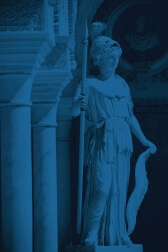 A statue of Minerva stands among columns in a well-lit hall. The statue wears a helmet and dress, and holds a spear.