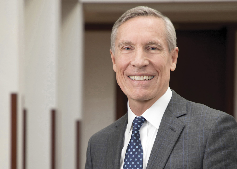 A headshot of David W. Oxtoby, a man with short gray hair. Oxtoby wears a white dress shirt with a navy blue tie and gray suit. Photo by Martha Stewart Photography.