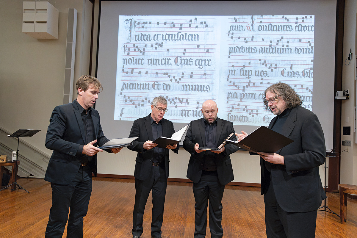 Four men in formal clothing singing in harmony. 