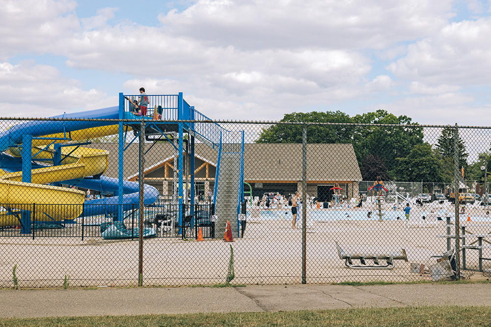 A public pool, including a blue and yellow waterslide, with people ready to use the slide. 