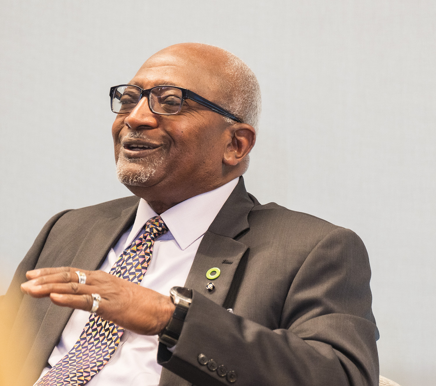 A panelist in a suit and glasses smiles mid-conversation. 