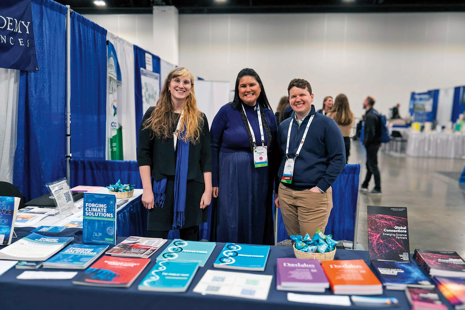 Carson Bullock, L. Kealoha Fox, and Leo Curran stand together in front of a table of colorful publications.