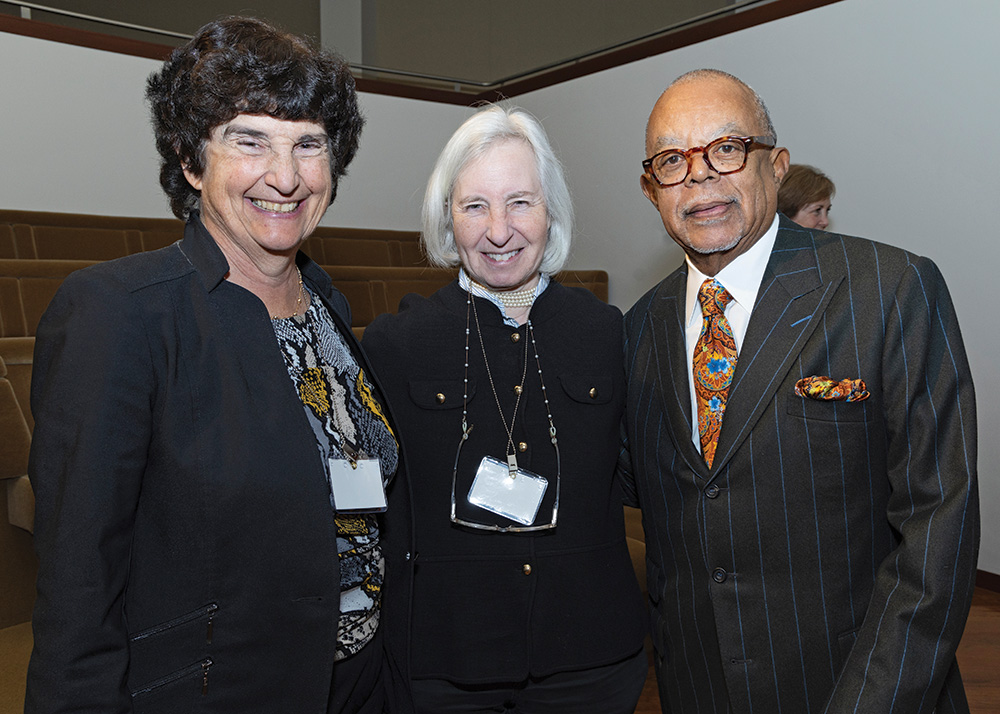 Three formally dressed members pose and smile in an auditorium. 