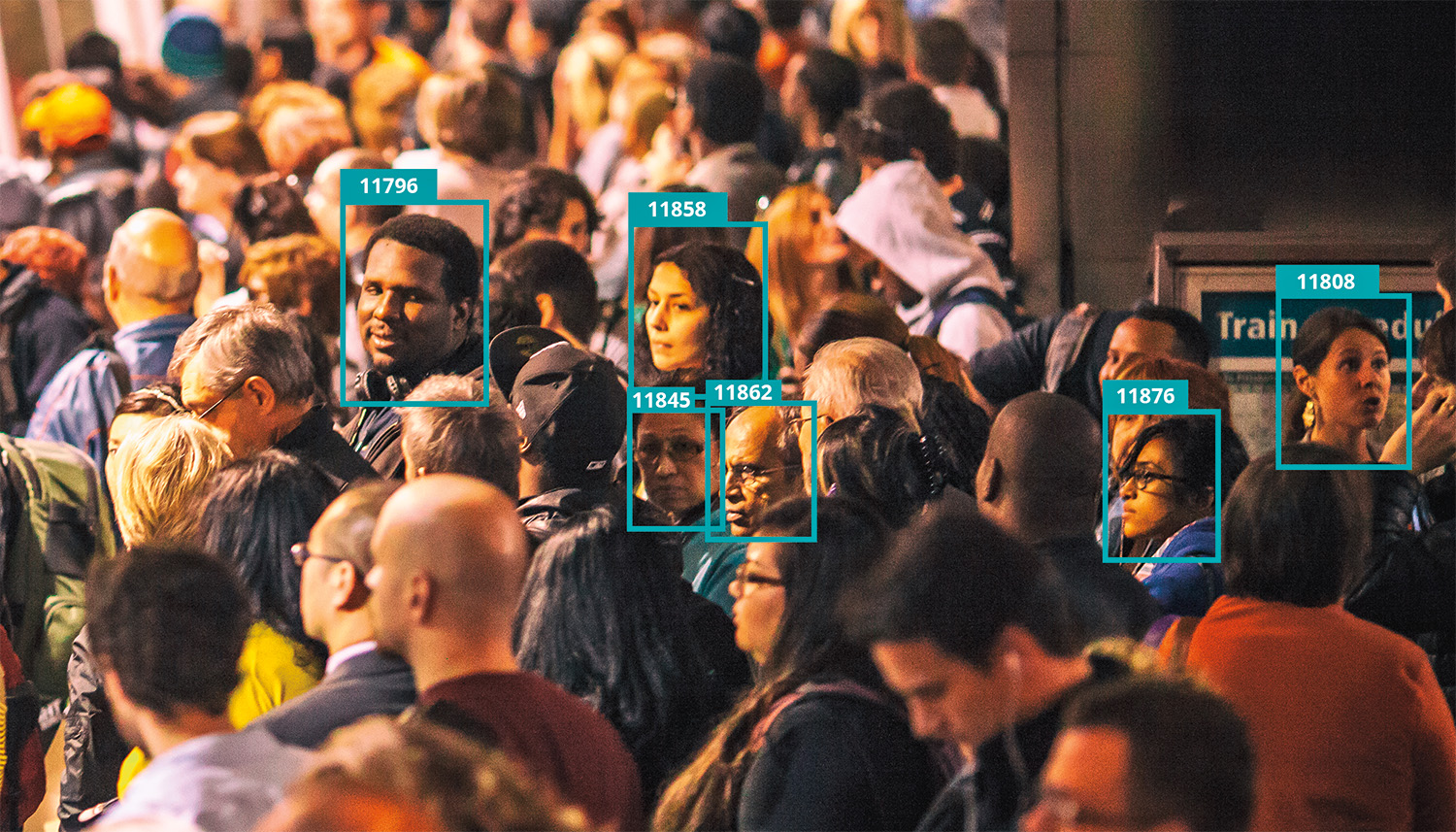 A crowded subway platform shows several commuters turning to face the viewer. Their heads are surrounded by digital boxes that label each an arbitrary number, implying categorization by facial recognition software. The commuters appear to be of various races and ages.