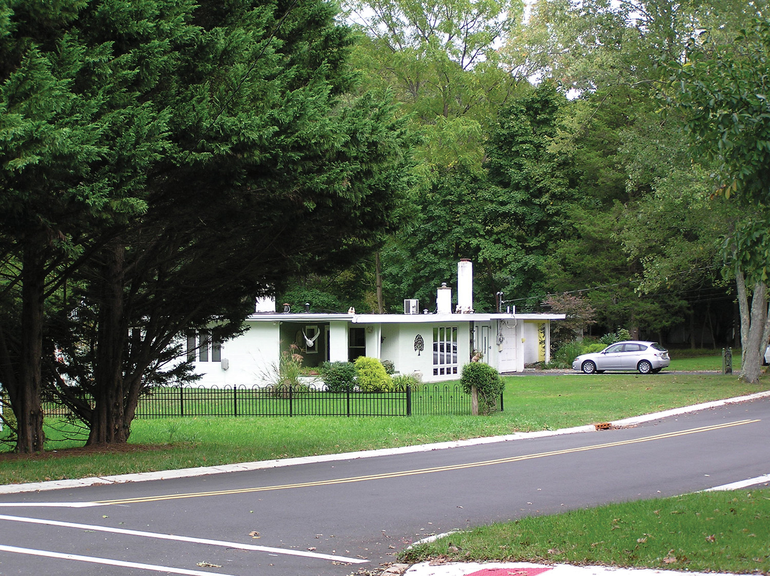 A white single-story house surrounded by trees, with a car parked in the driveway.