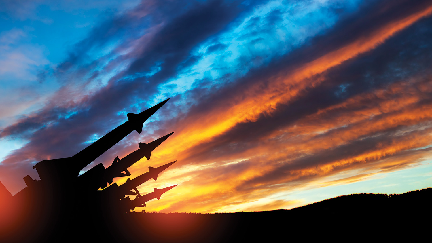 Four missiles pointed upwards against a sky at sunset, showing hues of blue, brown, orange, and yellow.