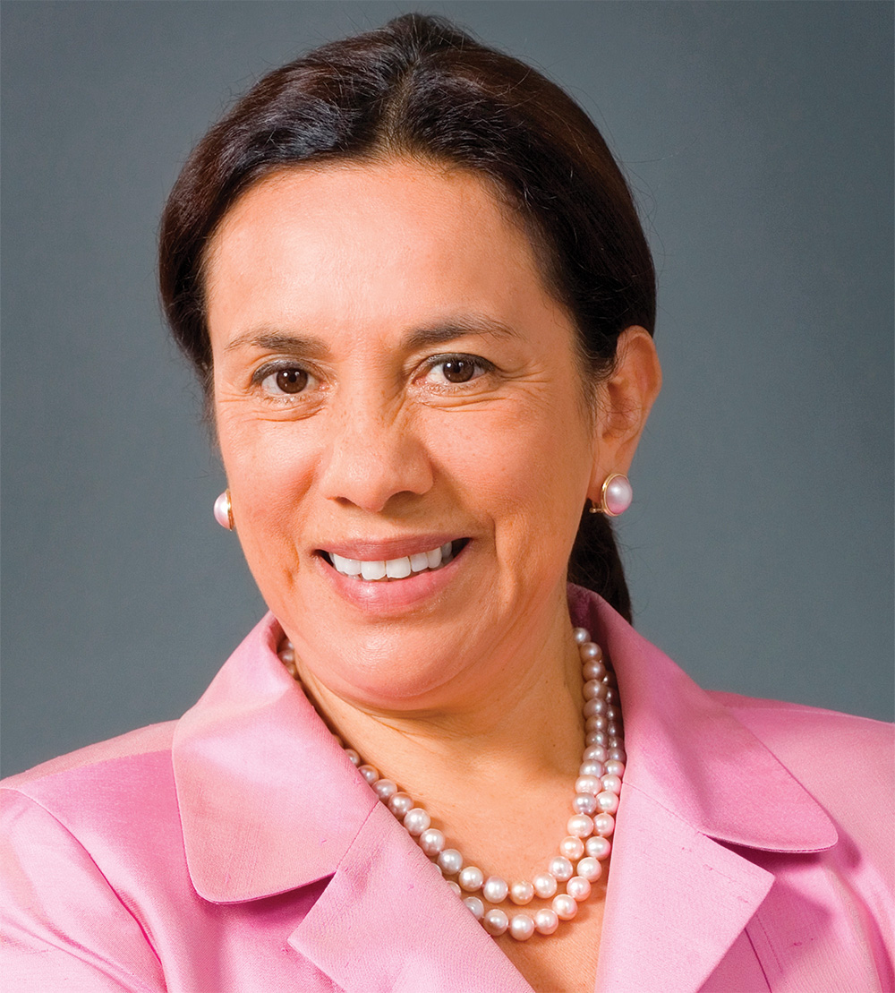 A photograph of Antonia Hernández, a person with brown skin and straight long brown hair. She faces the camera and smiles.