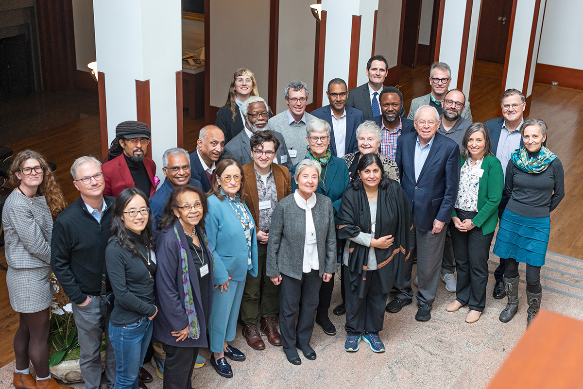 A group of approximately 25 people posing for a photo inside the Academy. The group includes people of varying ages, standing in a semicircle and smiling at the camera.