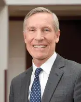 A headshot of David W. Oxtoby, a man with short gray hair. Oxtoby wears a white dress shirt with a navy blue tie and gray suit. 