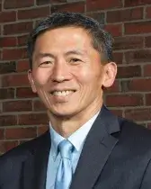 Headshot of Goodwin Liu, who has tan skin and short black hair. He wears a gray suit, blue tie, and faces the viewer smiling.