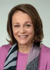 A headshot of Louise Henry Bryson, a person with pale skin, blue eyes, and shoulder-length brown hair. She wears business attire, faces the viewer, and smiles.