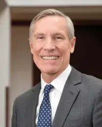 A headshot of David W. Oxtoby, a man with short gray hair. Oxtoby wears a white dress shirt with a navy blue tie and gray suit. 