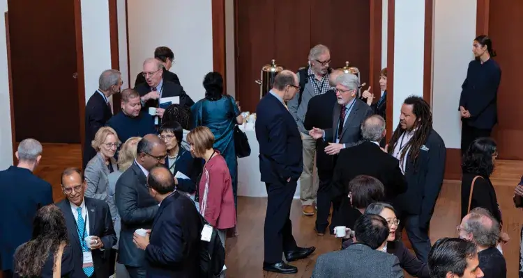 A large group of people in formal attire are engaged in conversation at a social gathering at the headquarters of the American Academy of Arts and Sciences.