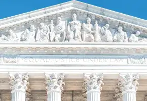 The relief sculptures on the pediment of Supreme Court Building on a sunny day. Beneath the states are the words “Equal Justice Under Law.”