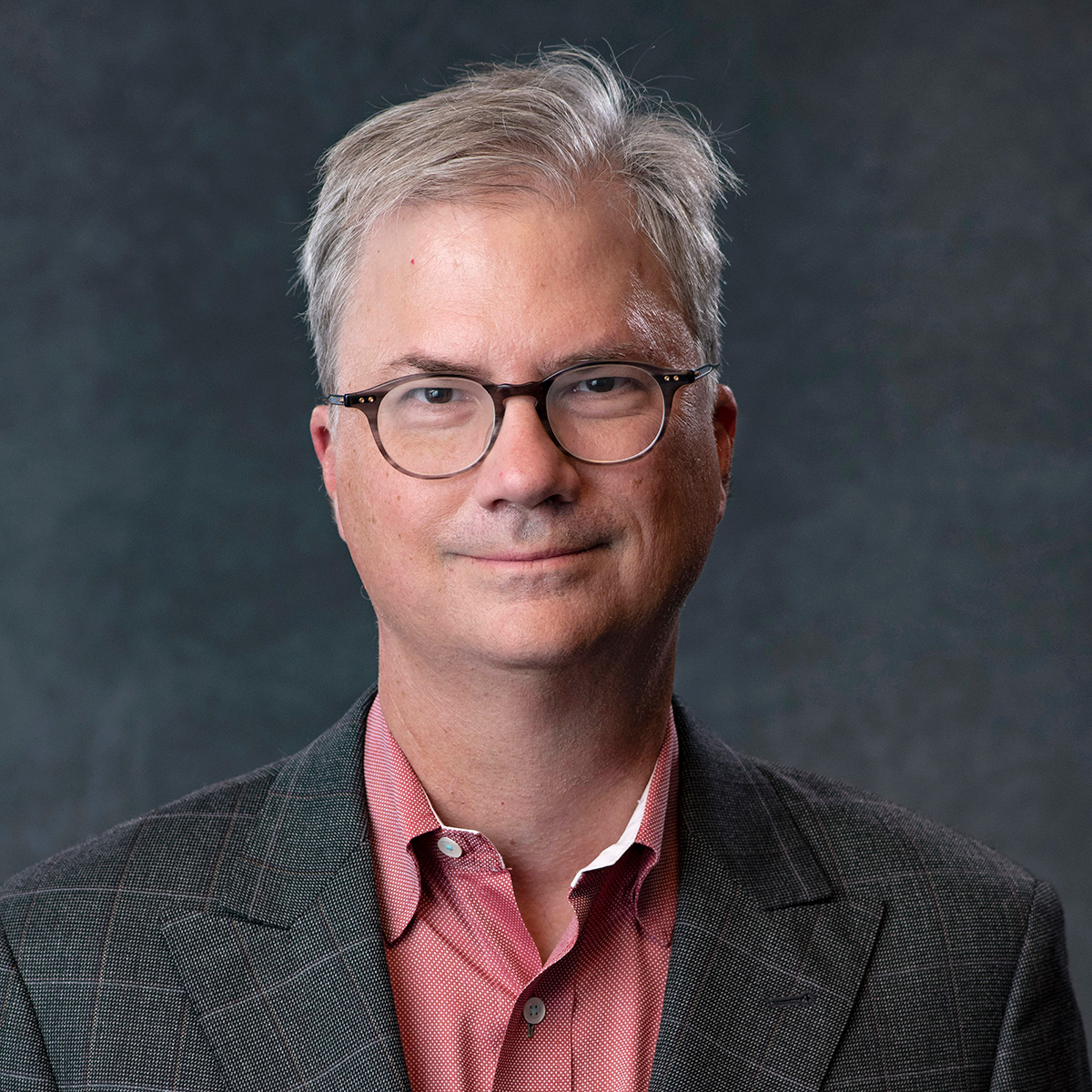 A photo of Holden Thorp, a light-skinned man wearing glasses, a gray plaid blazer, and a red button-down shirt. He has short gray hair and is smiling at the viewer.